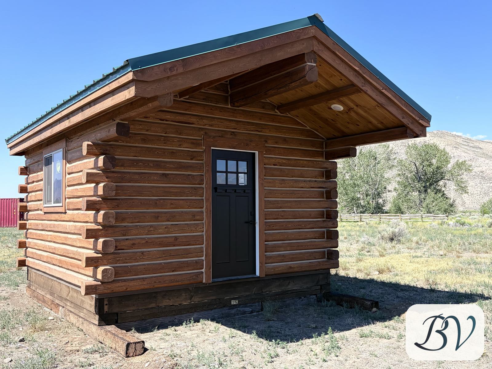Front three-quarter view of the log cabin showing the deep roof overhang, black door and protruding log ends
