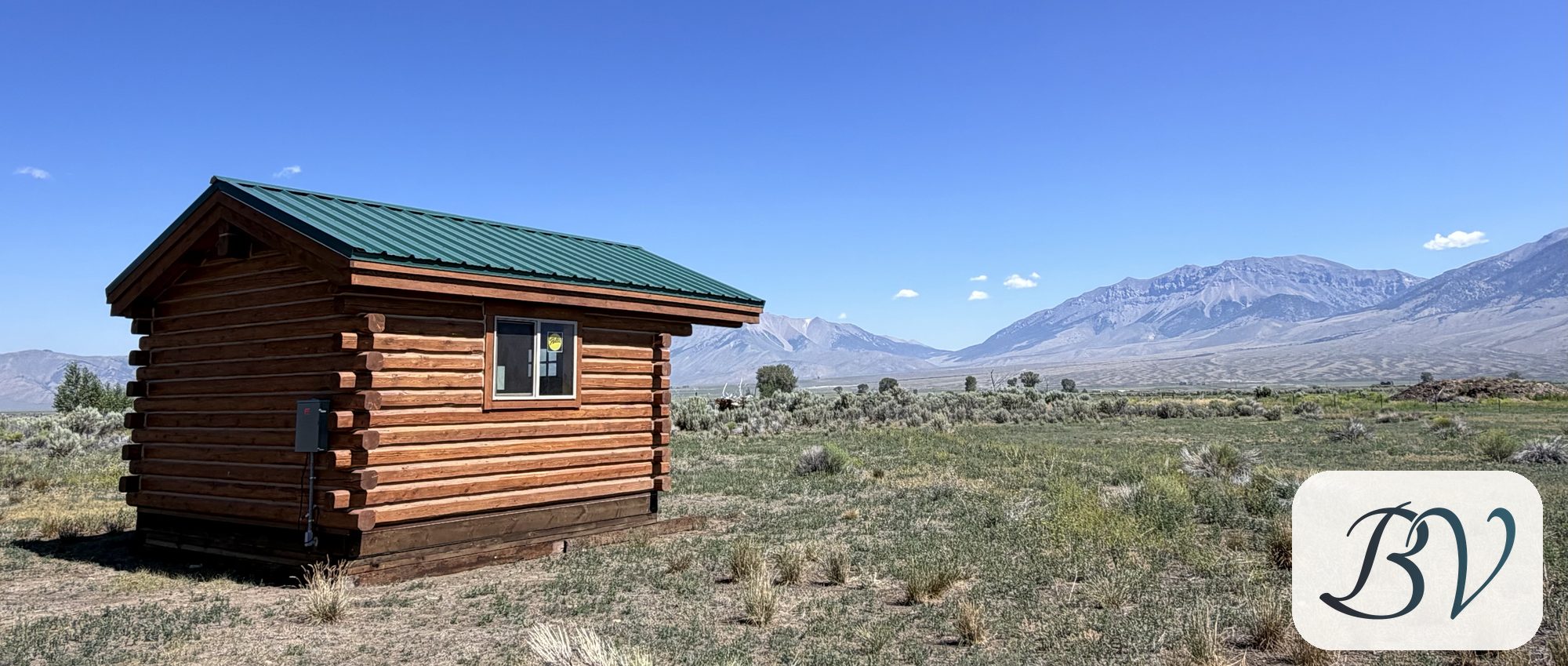 The log cabin standing in sagebrush under a clear sky, the Lost River Range running across the valley behind it