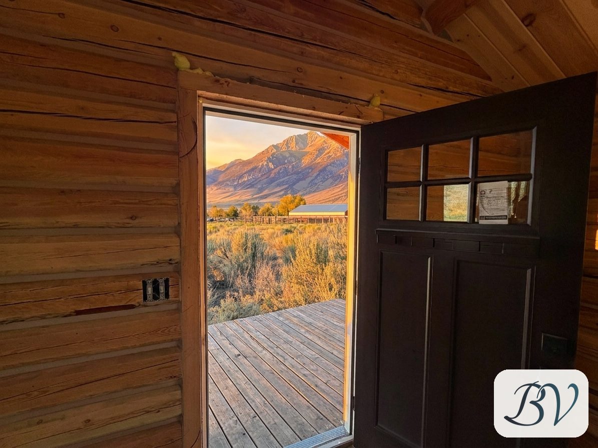 Looking out the open cabin door across the deck to the Lost River Range at sunset, with insulation foam still visible above the door frame